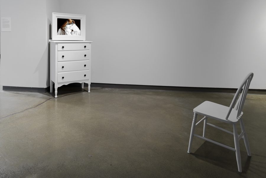 White wood dresser and chair stand opposite each other. Mirror on top of dresser shows the reflection of a woman.